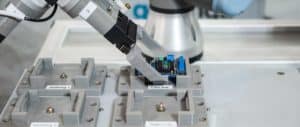 Bild eines Pick and Place Verfahrens mit Elektronikteilen. Roboterarm greift Elektronikbauteil.